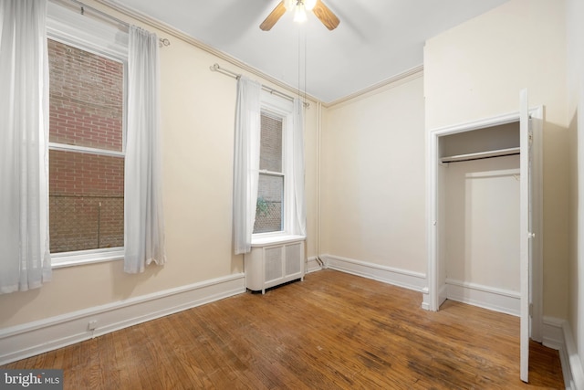 unfurnished bedroom featuring ornamental molding, a ceiling fan, hardwood / wood-style flooring, radiator heating unit, and baseboards