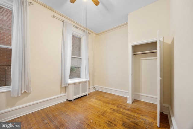 unfurnished bedroom with a ceiling fan, hardwood / wood-style floors, radiator heating unit, crown molding, and baseboards