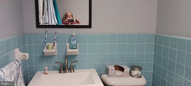 half bathroom with toilet, tile walls, and a sink