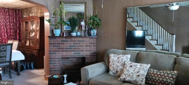 carpeted living area featuring stairway, arched walkways, wooden walls, and ceiling fan