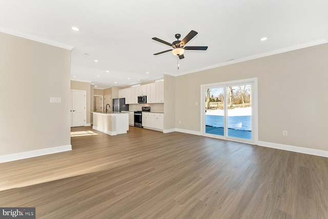 unfurnished living room with a sink, wood finished floors, baseboards, and ornamental molding