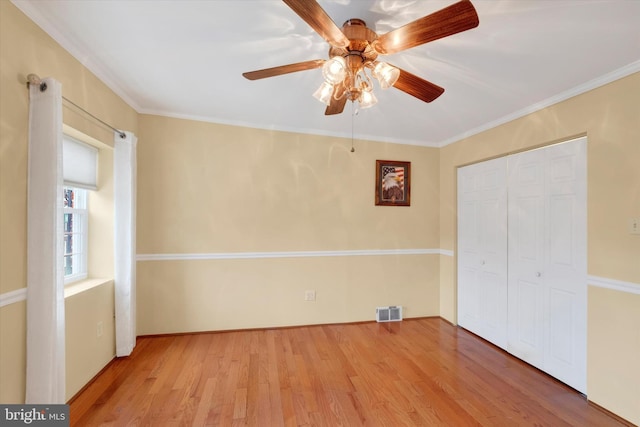 unfurnished bedroom featuring visible vents, a closet, wood finished floors, and crown molding