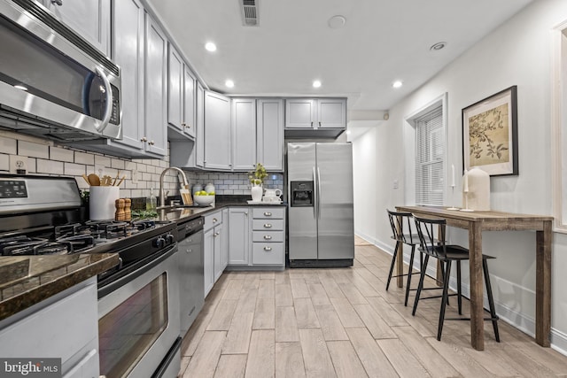 kitchen with visible vents, decorative backsplash, appliances with stainless steel finishes, light wood-style floors, and a sink