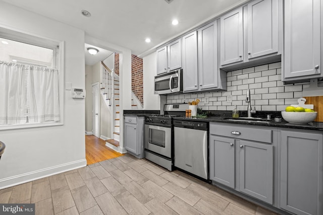 kitchen with backsplash, gray cabinets, stainless steel appliances, and a sink