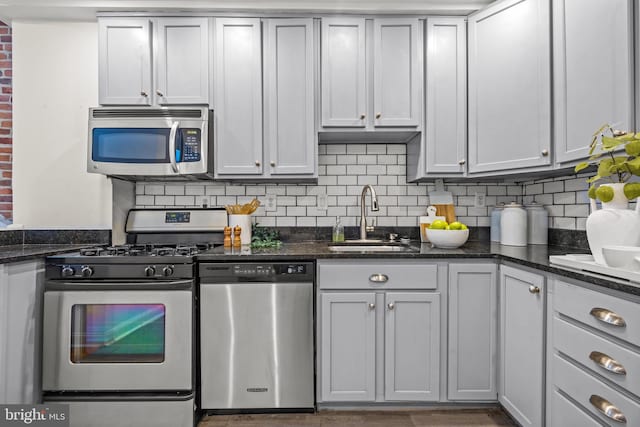 kitchen featuring decorative backsplash, appliances with stainless steel finishes, dark stone counters, and a sink