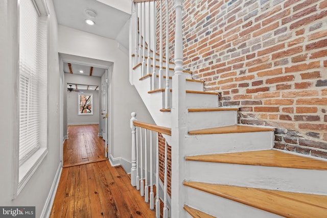 stairway featuring hardwood / wood-style floors, baseboards, and brick wall