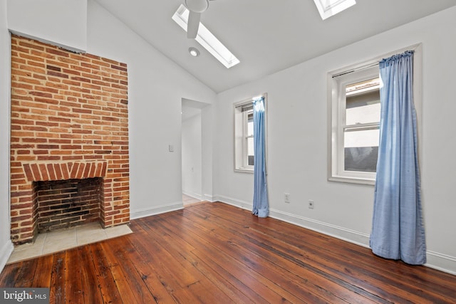 unfurnished living room with vaulted ceiling with skylight, a brick fireplace, baseboards, and hardwood / wood-style floors