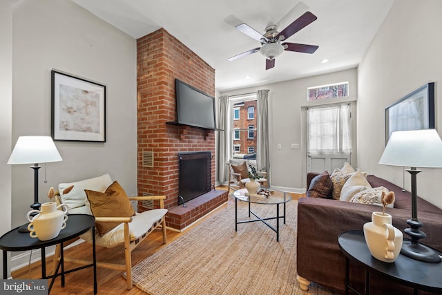 living area with a brick fireplace, baseboards, light wood-type flooring, recessed lighting, and a ceiling fan