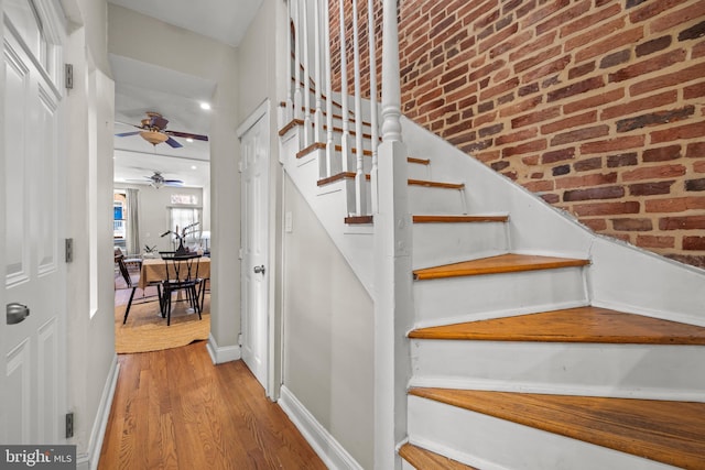 stairs with wood finished floors, baseboards, and brick wall