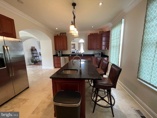 kitchen featuring a wealth of natural light, an island with sink, stainless steel appliances, arched walkways, and crown molding