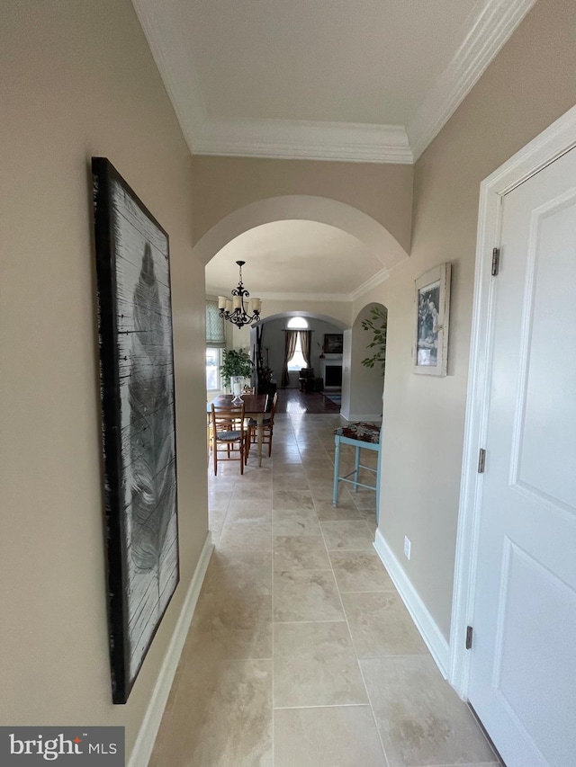 hallway featuring light tile patterned floors, baseboards, arched walkways, ornamental molding, and a notable chandelier