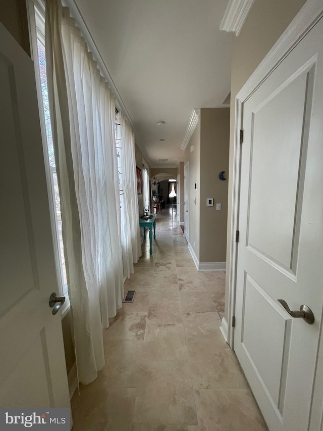 hallway with crown molding, baseboards, arched walkways, and a healthy amount of sunlight