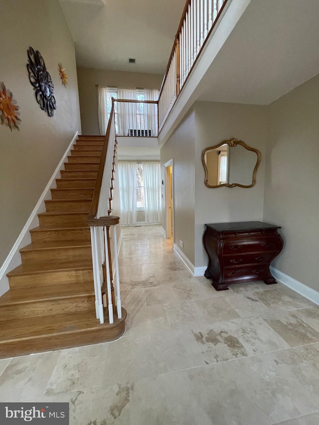 stairway with visible vents, baseboards, and a towering ceiling