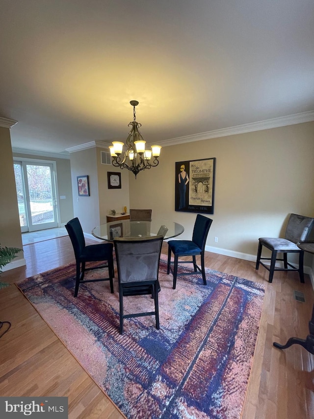 dining area with a notable chandelier, crown molding, visible vents, and wood finished floors