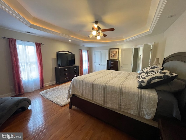 bedroom with visible vents, a raised ceiling, baseboards, and wood finished floors