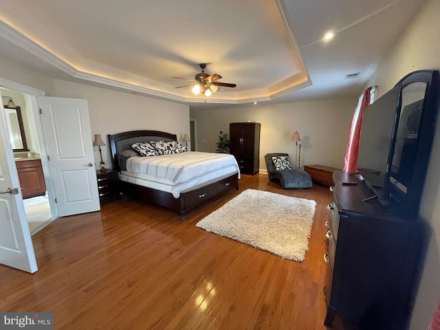 bedroom with ceiling fan, a tray ceiling, visible vents, and wood finished floors