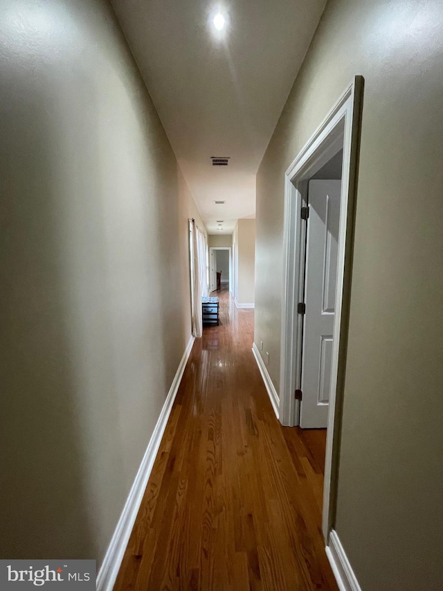 hall featuring visible vents, baseboards, and wood finished floors