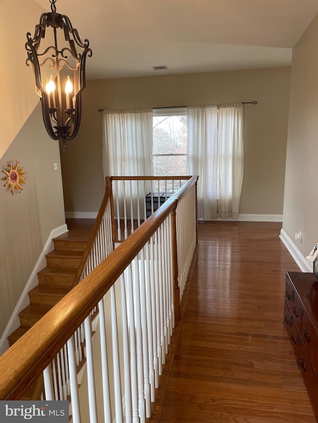 corridor featuring visible vents, baseboards, an inviting chandelier, and wood finished floors