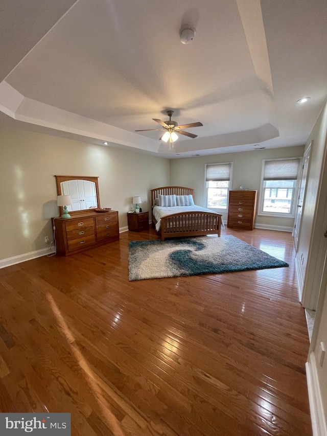 unfurnished bedroom with baseboards, a raised ceiling, and wood-type flooring