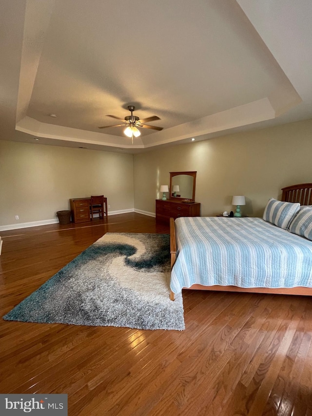 bedroom with baseboards, a raised ceiling, wood-type flooring, and a ceiling fan