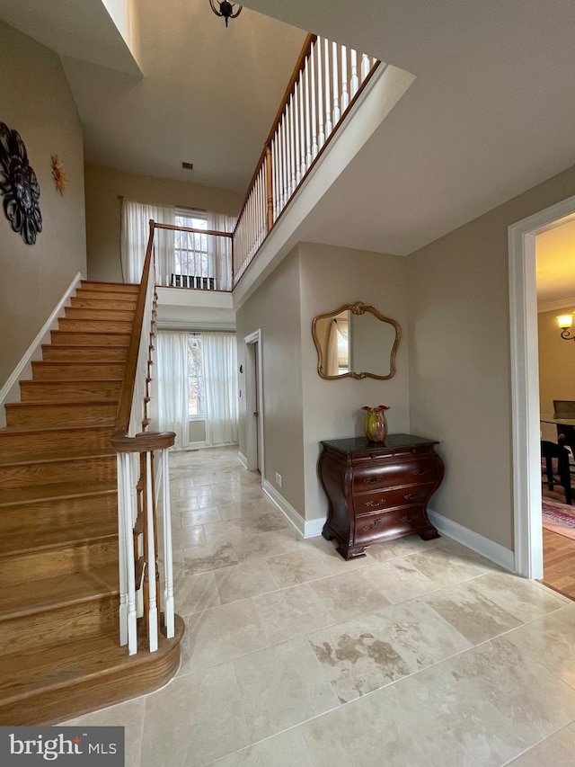 foyer entrance with stairs, a towering ceiling, and baseboards