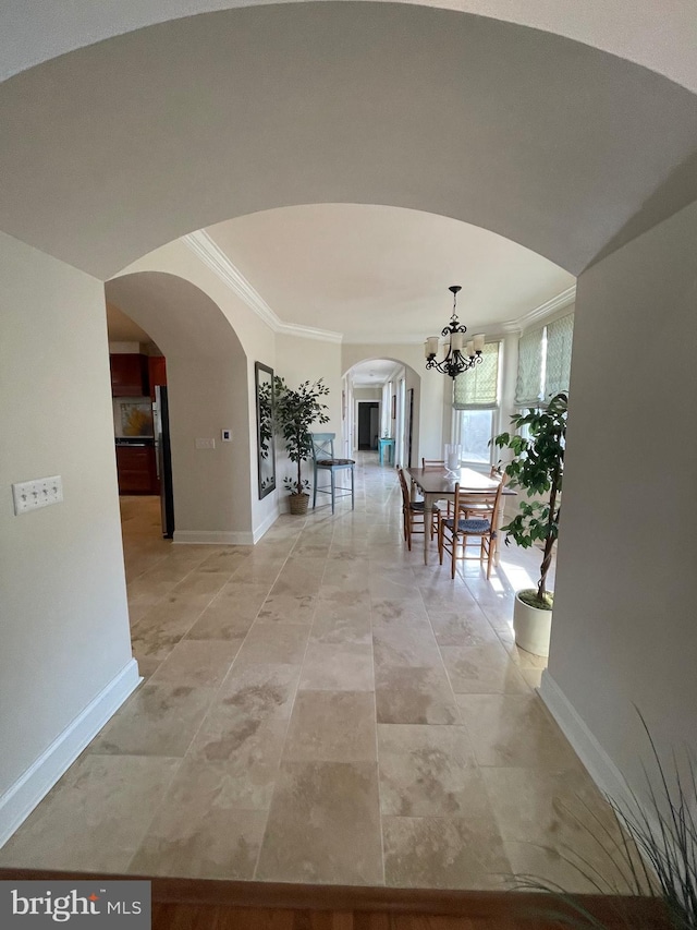 interior space featuring arched walkways, a chandelier, crown molding, and baseboards