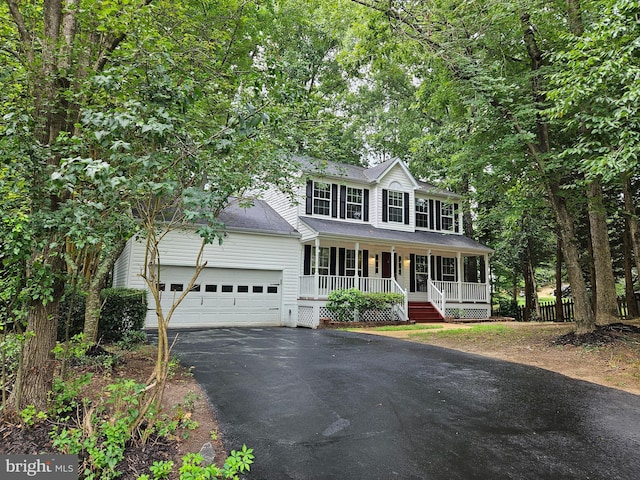 colonial-style house with aphalt driveway, a porch, an attached garage, and a shingled roof