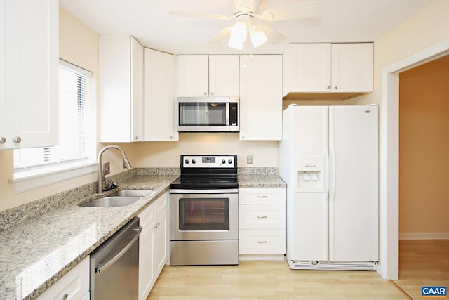 kitchen with light stone countertops, stainless steel appliances, light wood-style floors, white cabinetry, and a sink