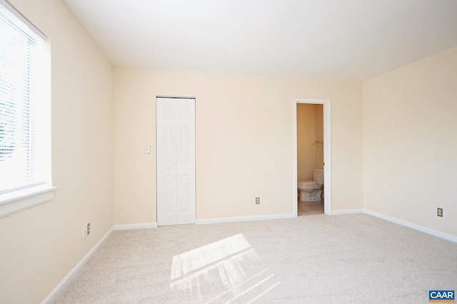 unfurnished bedroom with a closet, light colored carpet, ensuite bathroom, and baseboards