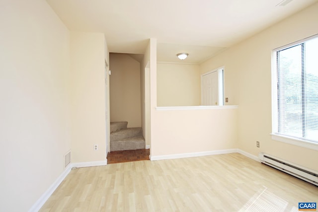 spare room with visible vents, a baseboard heating unit, baseboards, stairway, and wood finished floors