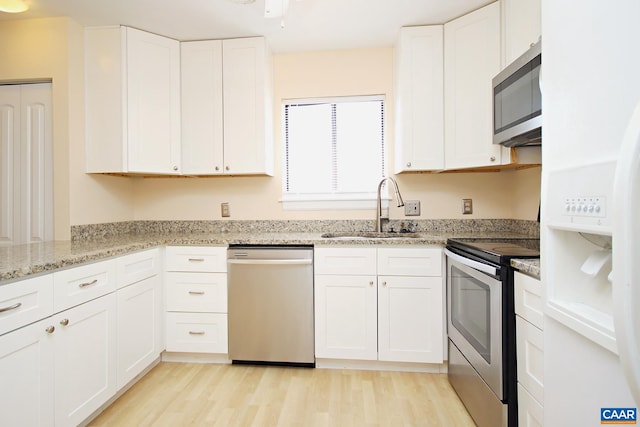 kitchen featuring light stone counters, a sink, white cabinets, light wood-style floors, and appliances with stainless steel finishes