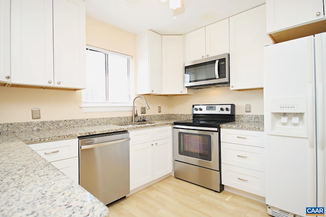 kitchen with light stone countertops, light wood-style flooring, appliances with stainless steel finishes, white cabinets, and a sink