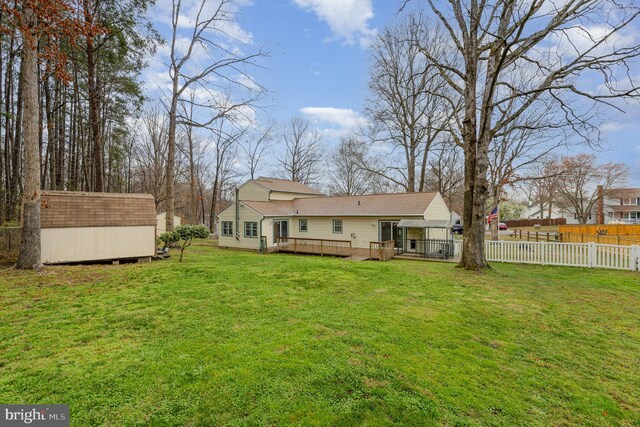 rear view of property featuring an outdoor structure, fence, a wooden deck, a storage unit, and a yard