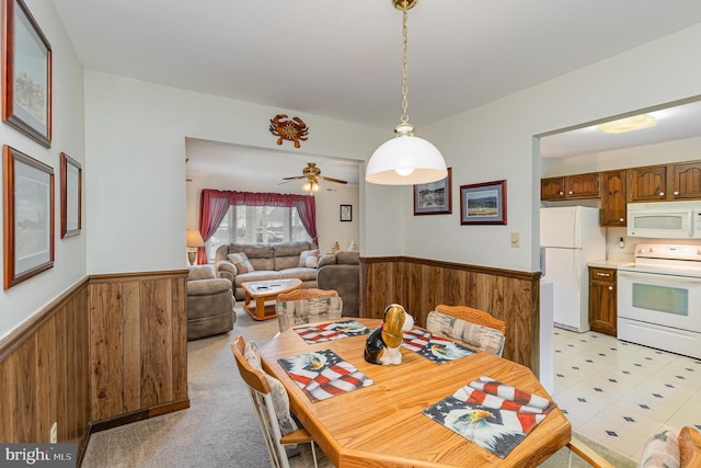 dining area featuring a ceiling fan, a wainscoted wall, and wooden walls