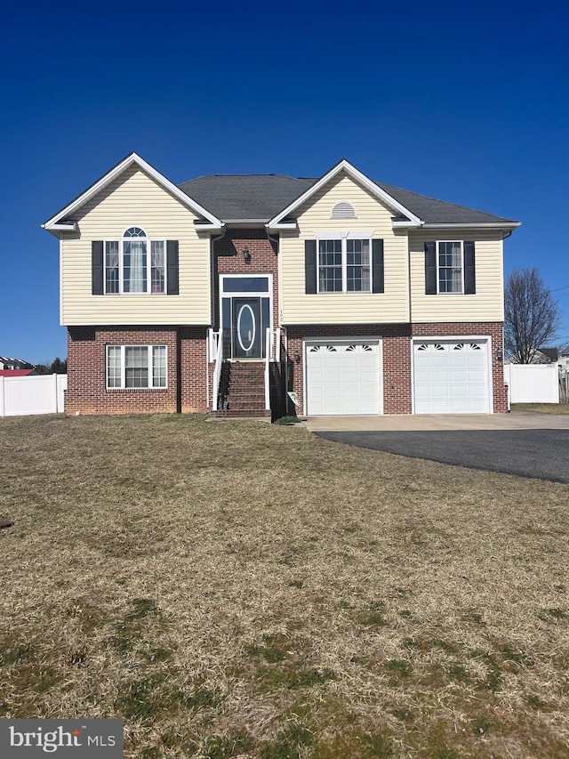 raised ranch with brick siding, a front lawn, fence, aphalt driveway, and an attached garage