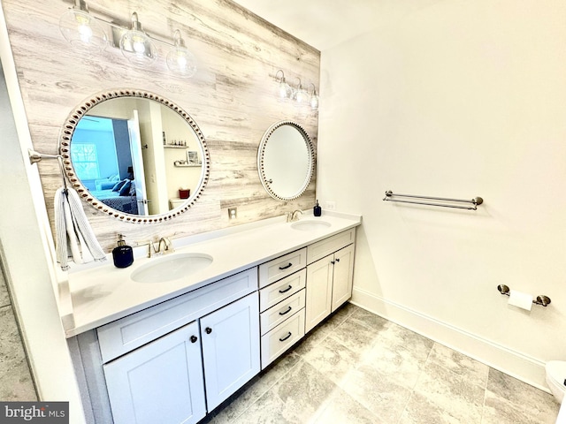 full bath featuring double vanity, ensuite bathroom, baseboards, and a sink