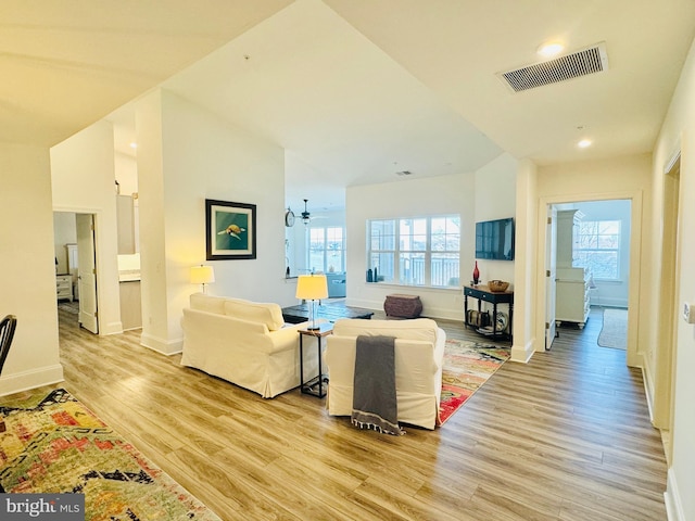 living area featuring light wood-type flooring, visible vents, baseboards, and a ceiling fan