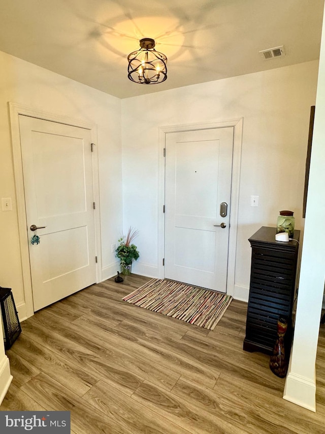 foyer entrance with visible vents, baseboards, an inviting chandelier, and wood finished floors