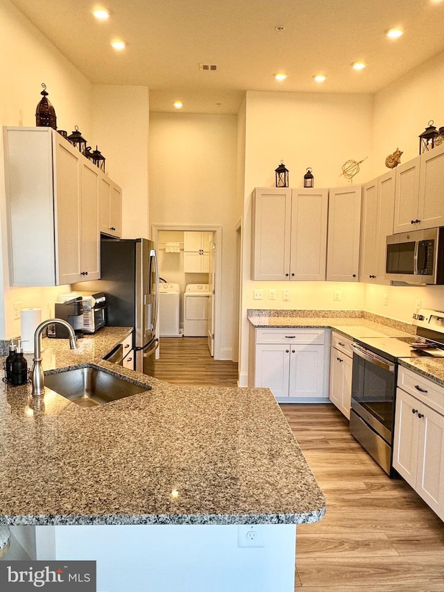 kitchen featuring washing machine and dryer, a high ceiling, stone countertops, stainless steel appliances, and a sink