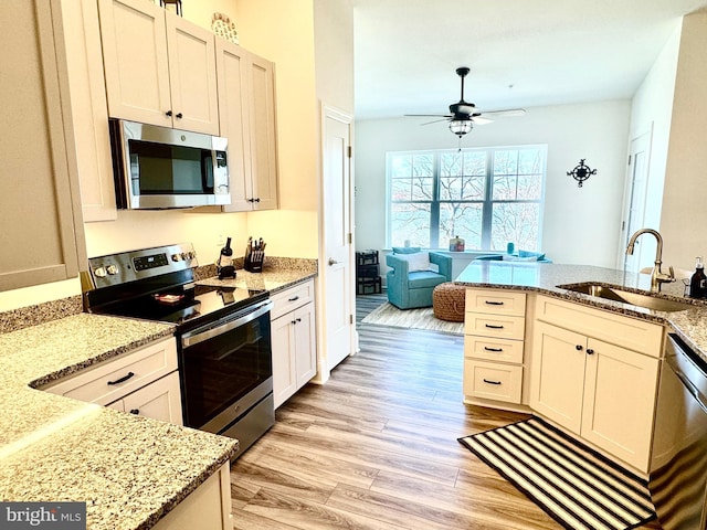 kitchen with a sink, stainless steel appliances, light stone counters, and light wood-style flooring