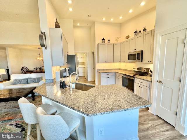 kitchen with light stone counters, a peninsula, a towering ceiling, stainless steel appliances, and a sink