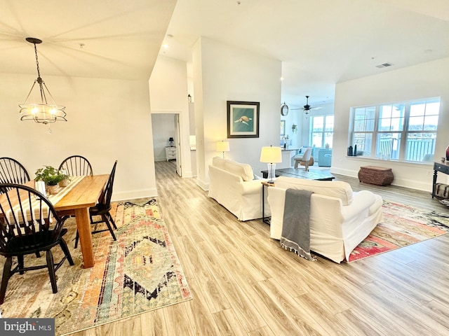 living room with light wood finished floors, visible vents, baseboards, lofted ceiling, and an inviting chandelier