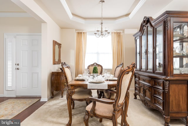 dining space with a notable chandelier, baseboards, a tray ceiling, and ornamental molding