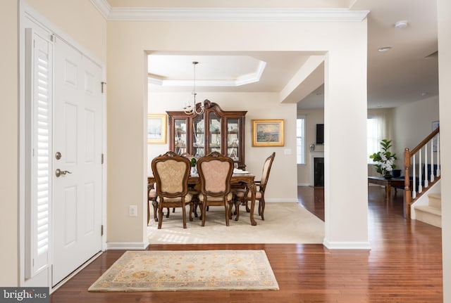 foyer entrance with dark wood-style floors, ornamental molding, stairs, a raised ceiling, and a chandelier