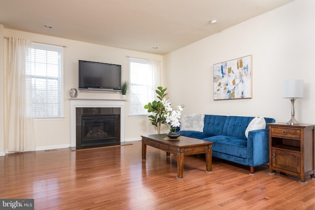 living area featuring recessed lighting, baseboards, a fireplace with flush hearth, and wood finished floors