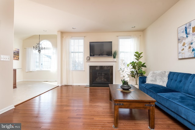 living area with baseboards, a fireplace with flush hearth, lofted ceiling, wood finished floors, and a notable chandelier