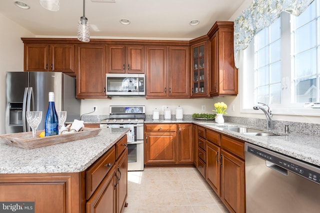 kitchen with a sink, light stone countertops, appliances with stainless steel finishes, and brown cabinets