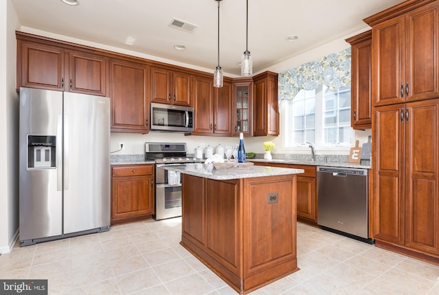 kitchen with visible vents, a kitchen island, light stone counters, appliances with stainless steel finishes, and hanging light fixtures