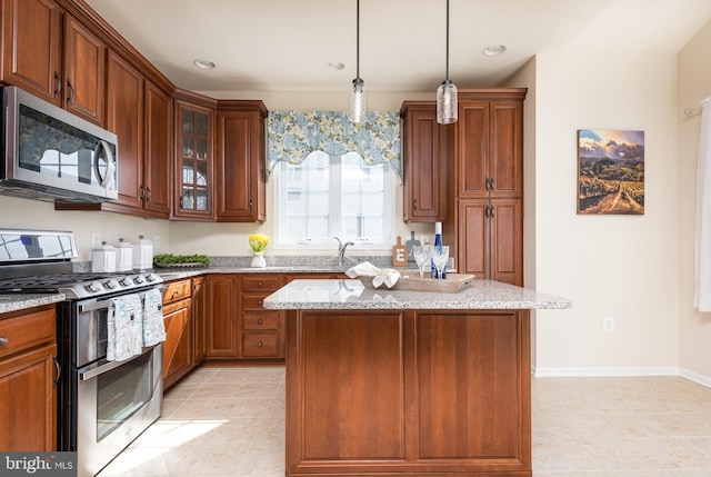 kitchen with pendant lighting, a kitchen island, appliances with stainless steel finishes, glass insert cabinets, and light stone countertops