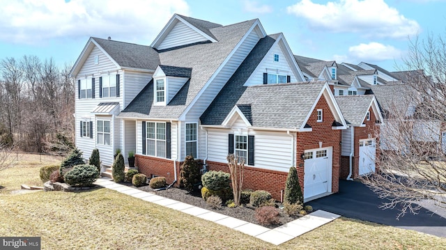 view of front of property featuring a front yard, driveway, brick siding, and roof with shingles